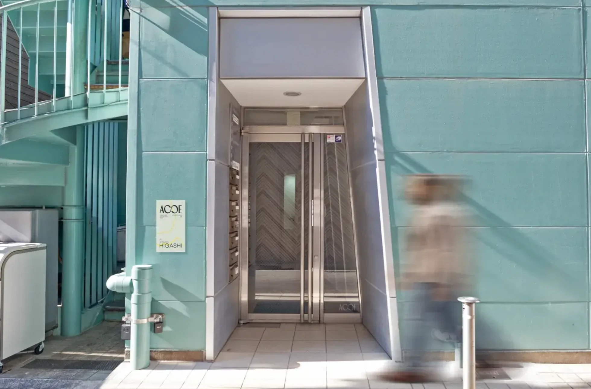 The entrance of an ACOE property: a teal facade, a glass door and an ACOE sign.